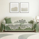 Green floral-patterned throw blanket on a sofa with two framed artworks on the wall.